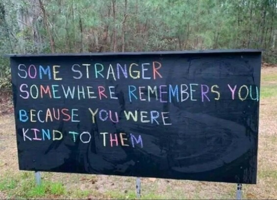 a black sign with pine trees in the background with multi-colored chalk writing on it that says "some stranger somewhere remembers you because you were kind to them"