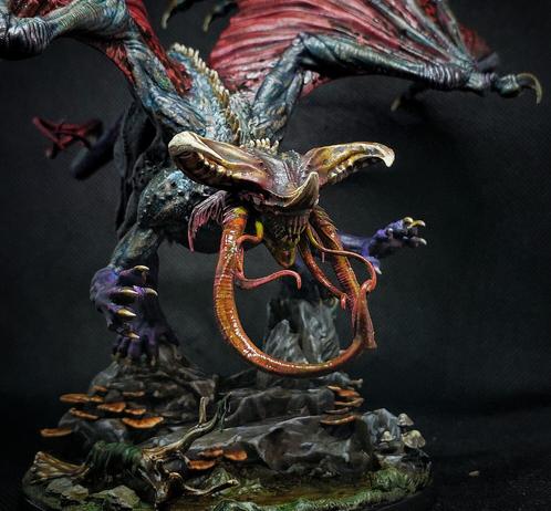 Photo of a painted miniature. A sickly blue grey Dragon with raw red wings & tentacles & six legs. The underbelly & legs are dark purple. It swoops down over a rocky, mushroom covered swamp, as if about to snatch prey.