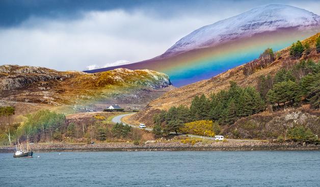 Snow topped hill with rainbow below.