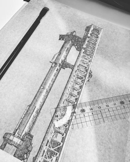 A black and white photo of the Starship/Falcon Super Heavy booster stack and launch tower with tracing paper, ruler and pencil lie on a light pad, partially traced.