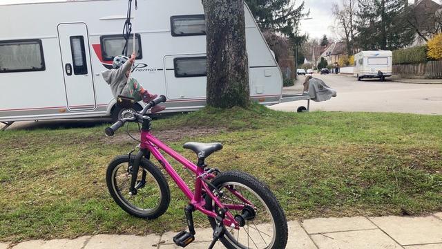 Fliederfarbenes Kinderfahrrad, dahinter Kind auf Schaukel.