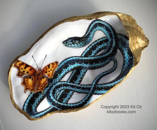a turquoise and black garter snake and a yellow and brown butterfly are painted inside an oyster shell with gold trim.