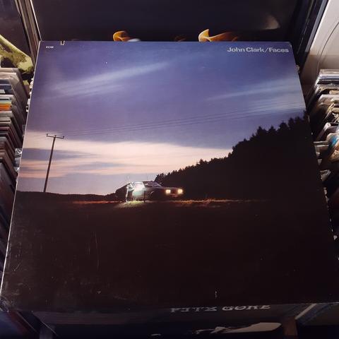Album cover features a photograph of a green, 1970s car stopped on a road at dusk. The car's headlights are on, and a ghostly figure holds the passenger door open. Above, the dying rays of the setting sun illuminate a bright blue sky and a white strip of cloud that stretches across the sky.