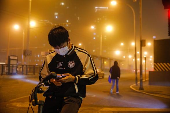 Chinese meteorological authorities issued a yellow warning for sandstorms and strong wind weather. A young man is walking along the dust shrouded streets at night. The streetlamps glow a bright yellow in the thick haze.