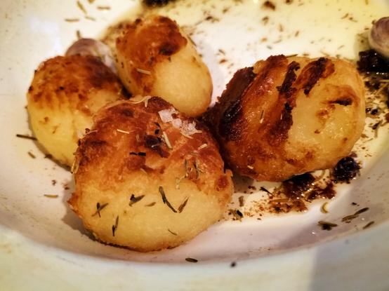 Four golden and crispy roast potatoes with garlic, rosemary and thyme in a white enamel roasting tin