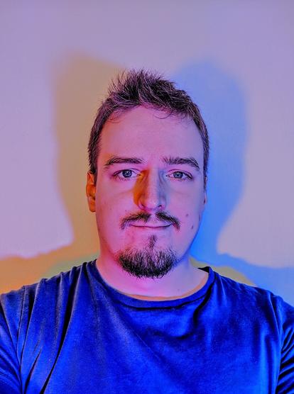 A selfie of the face of a man which projects two shadows on the wall behind.