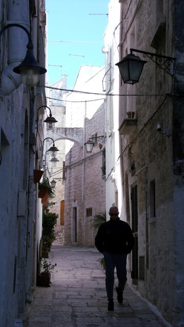 An alley, in a Southern Italian town, with a cool-looking, sunglasses-wearing gentleman walking towards the camera.