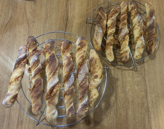 Eleven freshly baked cheese sticks are resting on two of my round cooling racks. Under the artificial kitchen light they look dark and almost slightly sad.