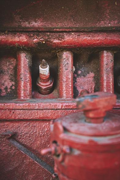 View of an old, formerly bright red tractor‘s engine block from the side. It has been off duty for a long while. The outer part of a spark plug can be seen near the center with a white thread where the cable used to be.