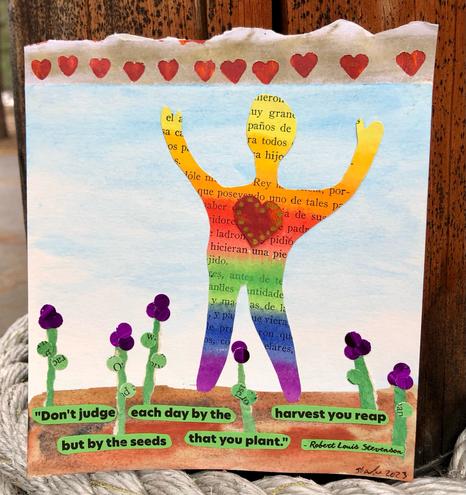 A rainbow striped figure with a raised, red heart stands in a field of purple flowers sprouting from green “seeds”. The seeds have a quote from Robert Louis Stevenson printed on the green paper which reads, “Don’t judge each day by the harvest that you reap but by the seeds that you plant.” The sky in the background is blue and at the top of the image is a row of gold and red hearts.