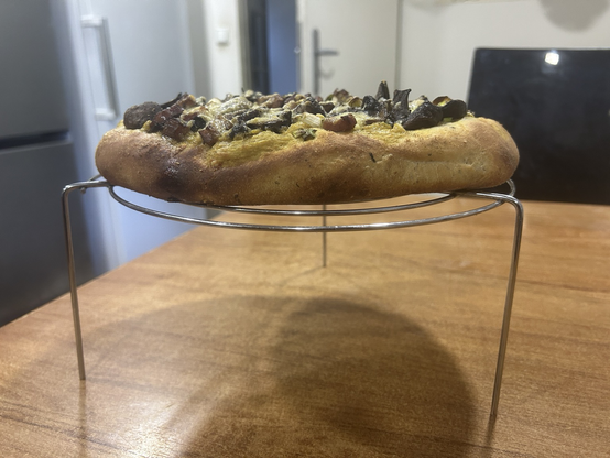 The pizza bread on my big round cooling rack, seen from the side; it's two to three times as thick as a normal pizza crust would be, which was the aim of the exercise. The crust is nicely browned but then it was baked for 12 minutes at 250°C/482°F