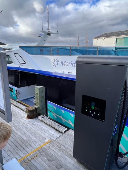 An electric ferry boat partly obscured by a charger it is plugged into