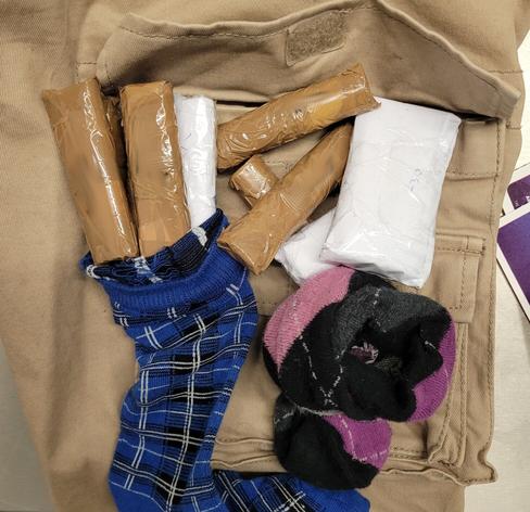 Umwickelt mit weißem und braunen Paketklebeband versteckte ein Mann Rollen von Geldscheinen in zwei verschieden farbigen bunten Strümpfen. im Bild liegen Rollen und Strümpfe auf einer beigen Hose.