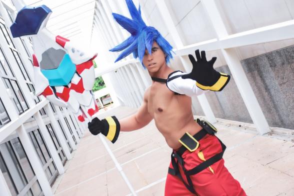 Galo Thymos cosplay from Promare by MelPool. Blue spiked wig, white, blue, red, and teal matoi staff, white arm sleeve, black and yellow gloves, black and yellow belt with pouches, red pants.