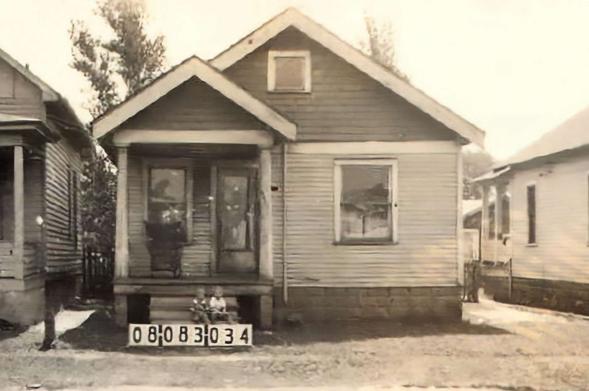 Sepia photograph of a house with two boys sitting on the step of the front porch.