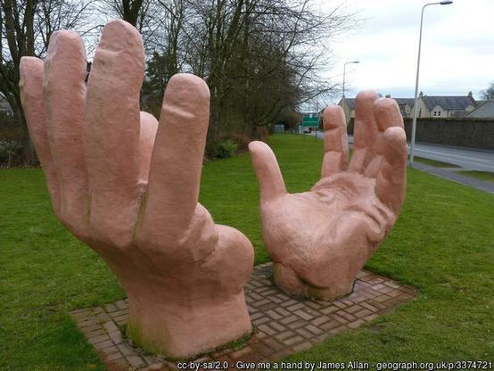 Childens play area in the form of two giant human hands sticking up out of the grass