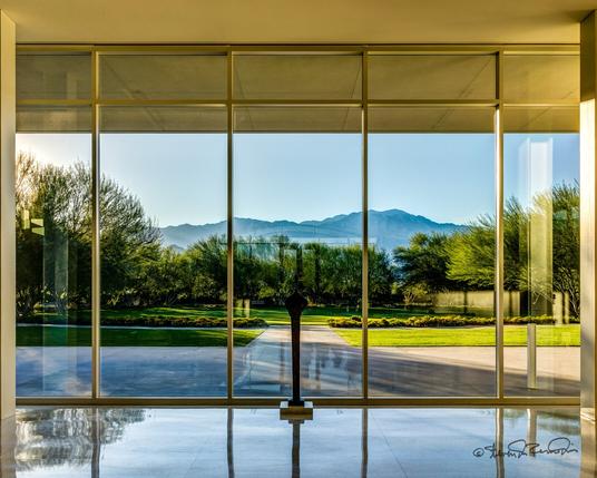 Five floor-to-ceiling windows overlook a manicured garden and distant desert mountains.