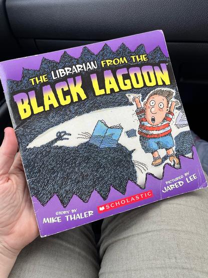 The cover of a book titled “The Librarian from the black lagoon”. The art features a big shadow with a book and a scared looking child.