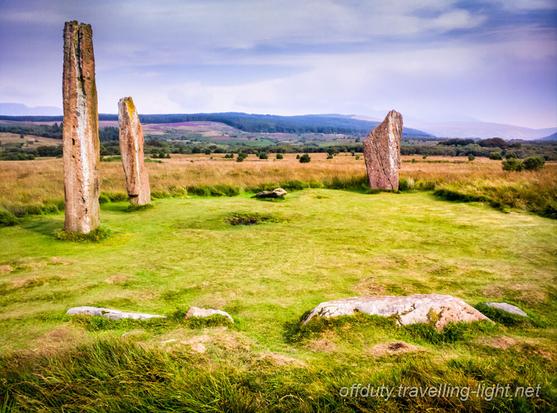 Three standing stones and two horizontal stones in a circle of grass on moorland.