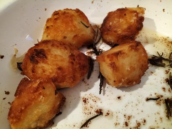 Five golden and crispy roast potatoes with garlic and rosemary in a white enamel roasting tin