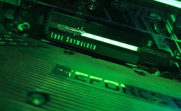 Photo showing an NVMe SSD drive installed in a computer. The drive has a lightsaber hilt on the left and a green RGB LED coming out of it with the words LUKE SKYWALKER printed below it. The entire image is cast in a green glow from the RGB lighting.