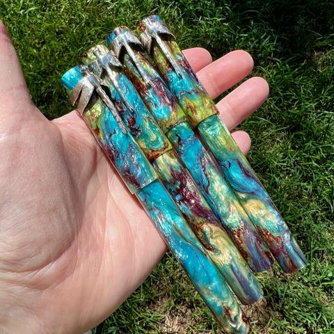 4 Scriptorium Pens Kelmscott Dragonfly Special Edition, held in maker’s hand above a green grass background.