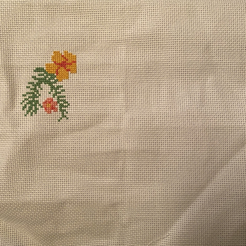 Partially finished cross stitch project with a small pink flower and a leaf, and a larger yellow flower above it.