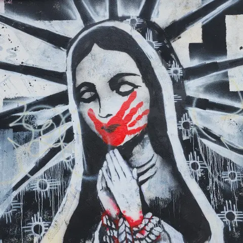 closeup of black and white mural of Tonantzin with a red handprint over mouth, hands bound with rope in traditional prayer position, and Zia symbols on robe instead of stars