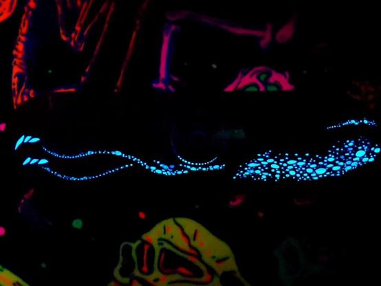 A brightly coloured skateboard painted with a Japanese Firefly Squid. Pictured on top of dinosaur bone carpet. The lights are off to show off the blue glow in the dark paint.
