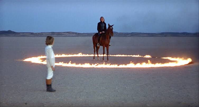 Horse in ring if fire near young child in white standing watching