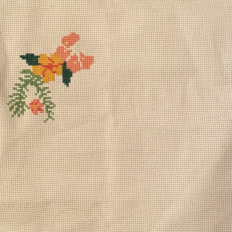 A partially finished cross stitch project. A large leaf with two pink flowers and a yellow flower.