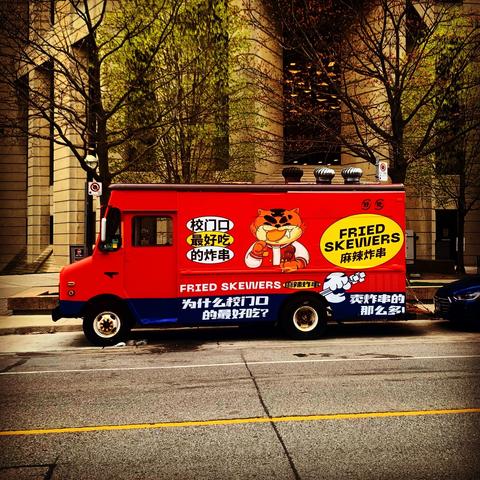 Food truck painted red, with Korean writing on it with Fried Skewers printed in English. There is a stylized anime type cat eating a skewer.