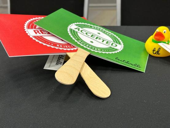 Hand held voting paddles showing green Accepted and red Rejected, sitting next to a rubber duck programmer with a Test Double logo