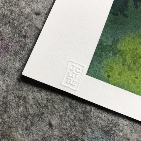 This is a photograph of the corner of one of my art prints. On the corner, there is a white border of the print, and in this white border is an embossed stamp. The stamp is my insignia with my name “JC Little”. If you were to touch it with your fingers, it would probably feel like a rectangle with some letters in the middle. The stamp is pressed into the paper from underneath so that you can feel it with your fingers. This gives the print authenticity so that you can know that it was done by the artist and approved. Certified authentic!