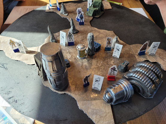 Tabletop RPG terrain showing a cavern with stalagmites and machinery inside along with several troops and a party of spacefaring adventurers.