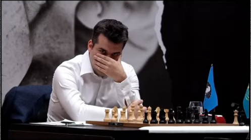A screenshot from the FIDE World Chess Championship stream. We see Ian Nepomniatchthi waiting at the chessboard. He's wearing a white shirt, and appears to be covering most of his face, lost in thought.