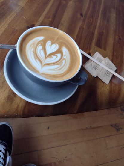 A cafe latte on a table with sugar and a stir stick.