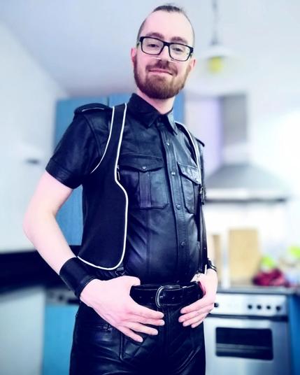 A young man with a tusk septum piercing wearing full leather smiling into the camera.
