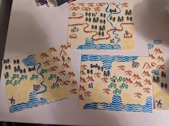 Three maps and a bookmark made with repeated stamp shapes in different colours. One shows a lake flowing into the sea with mountains to the east and farmland around the sea. Another shows a river flowing through a forest and over cliffs, also to the sea. Another shows a narrow land mass with water to the north and south and mountains in the middle.  The bookmark shows the sky, then mountains, then forest, then farmland.