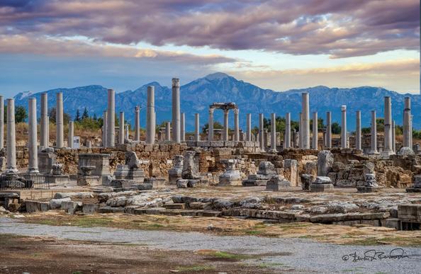 A mid-view of stone marketplace columns with #mountains in the distance under partly cloud skies.