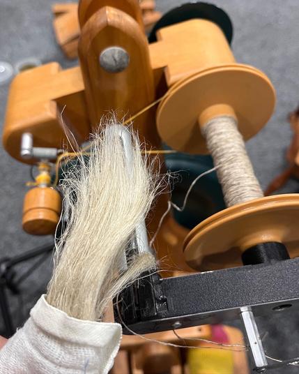 A hank of flax fiber wrapped in a white cloth. In the background is the top of a modern spinning wheel with a bobbin that has some flax yarn spun onto it.