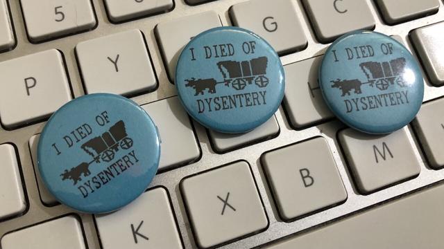 Blue button badges that say ‘I died of dysentery’ and have a bitmap image of an ox pulling a cart