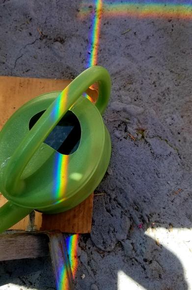 Rainbow prisms on green watering can & the ground.