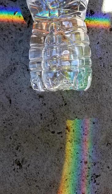 Multiple rainbow prisms on ground & water bottle.
