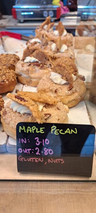 A row of maple pecan donuts which look decadent with cookies sitting atop them.  There's a bit of red espresso machine visible in the background as well.