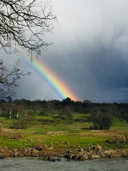 Vivid rainbow arcing down to green Earth above Sacramento River.