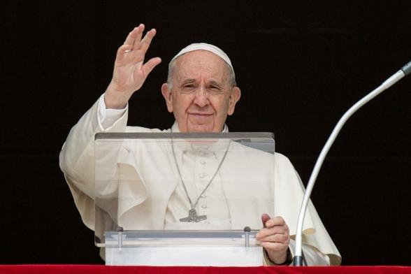 Pope Francis giving a benediction while standing behind a transparent lectern.