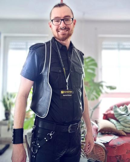 A young man in full leather with a septum ring and a plastic badge around his neck.