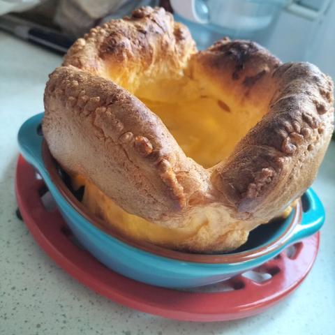 A large golden Yorkshire pudding in a blue ceramic bowl with handles either side that's on a red metal trivet