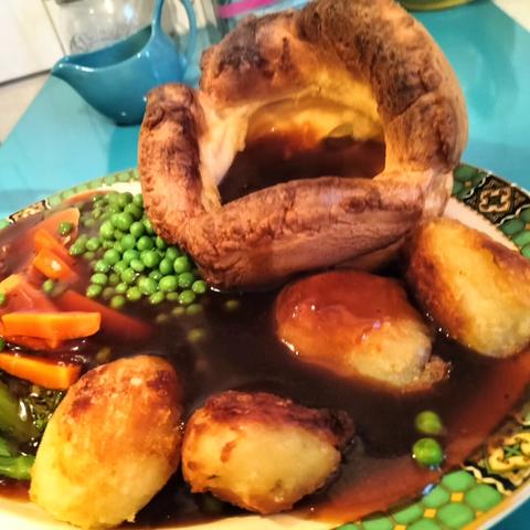 Roast dinner: large Yorkshire pudding filled with gravy, four golden and crispy roast potatoes, carrot batons, peas and gravy